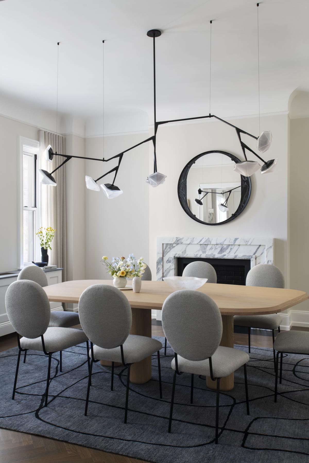 Myriad long glass chandelier with angular black frame and white geometric shades floating above an elegant oval dining table